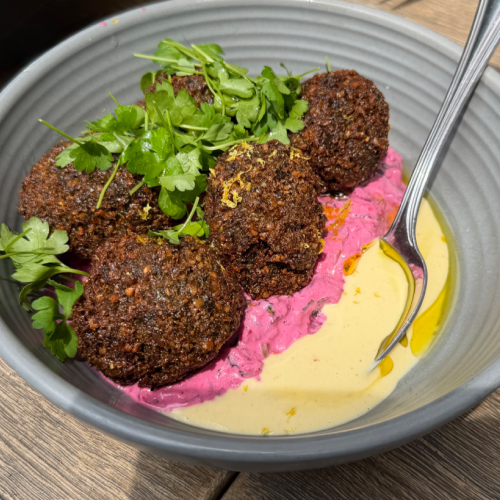 Crispy herb falafel served over vibrant beet yogurt with creamy tahini sauce and fresh herbs.