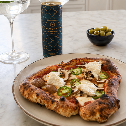 Wood-fired mushroom, jalapeño, and burrata pizza served with a Melograno Cucumber Lime Mojito cocktail on a marble tabletop.