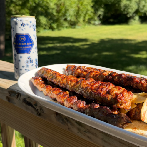 Persian Koobideh kebabs grilled over open flames and served with a Melograno Orange Blossom Martini on an outdoor table.